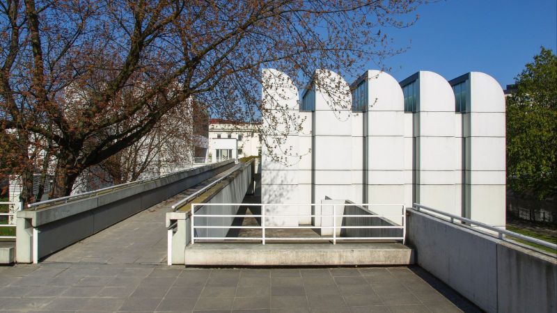 Außenansicht des Bauhaus-Archivs in Berlin mit markanten, gefalteten Dachformen. Moderner, weißer Gebäudekomplex am Wasser mit klaren Linien und minimalistischer Gestaltung.