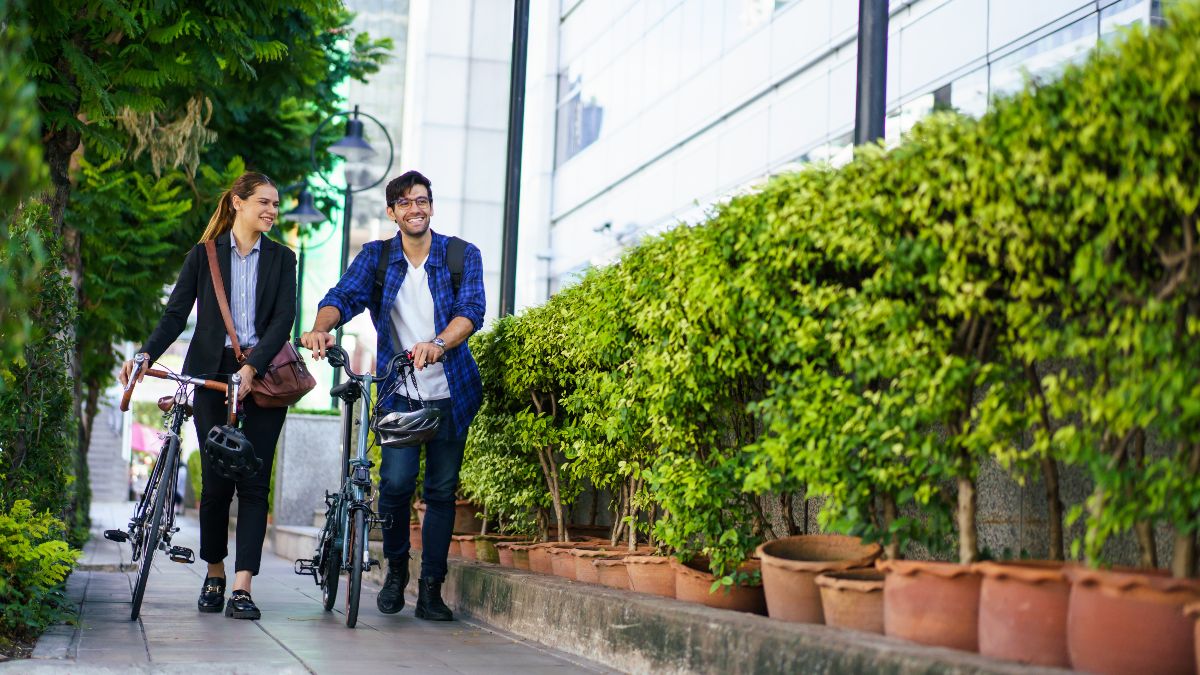 Zwei Personen gehen in einer Stadt an Büschen vorbei.