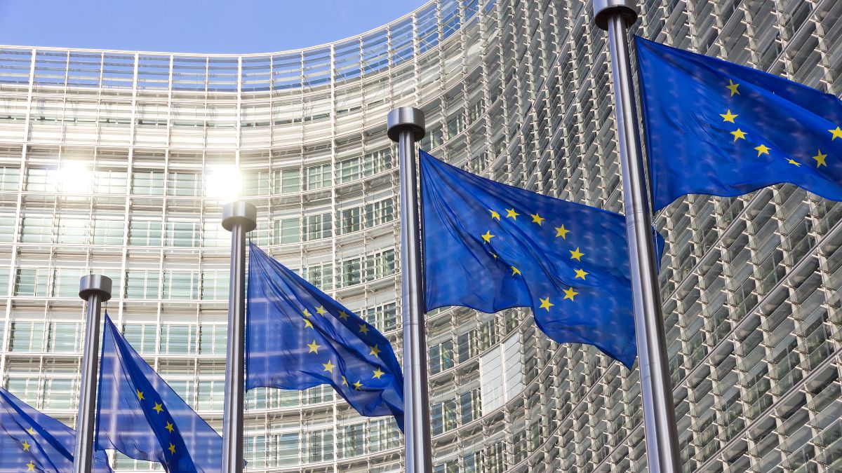 Bild des EU Kommissions Gebäude in  Brüssel mit Europa Fahnen im Vordergrund.