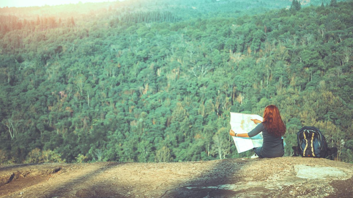 Frau sitzt vor einem Wald mit einer Karte in der Hand.