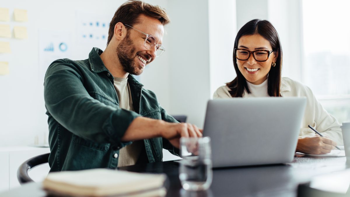 Zwei in einem Büro sitzende Geschäftsleute betrachten gemeinsam den Bildschirm eines offenen Laptops; Tastatur, Bildschirm und Hände sind deutlich sichtbar.