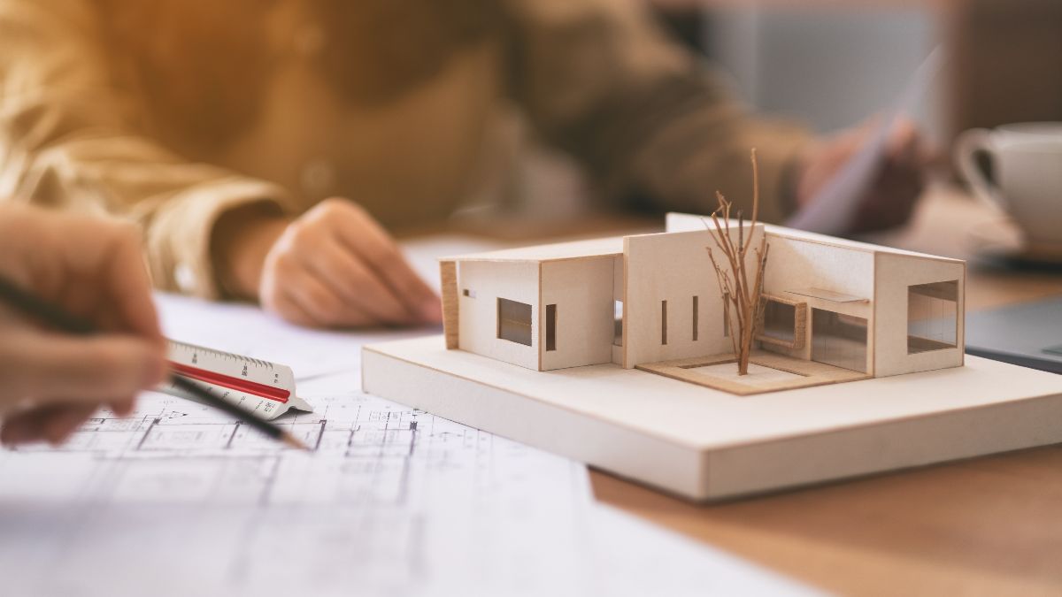 Mehrere Personen am Tisch mit einem physischen Architekturmodell, Bauzeichnungen und Papieren, die gemeinsam das Modell und Pläne im Büro betrachten und besprechen.